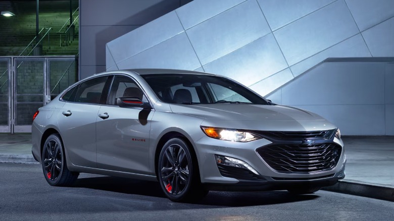 A silver 2025 Chevrolet Malibu parked under bright lights in an urban setting.