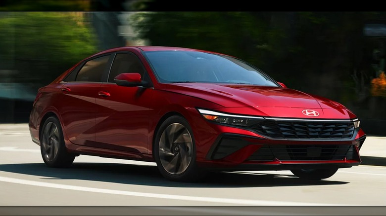 A red 2025 Hyundai Elantra sedan driving through a curve on a city street.
