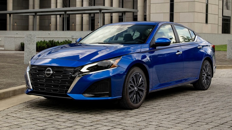 A blue 2025 Nissan Altima SV Special Edition parked on a cobblestone surface in front of a modern building with tall columns and large windows.