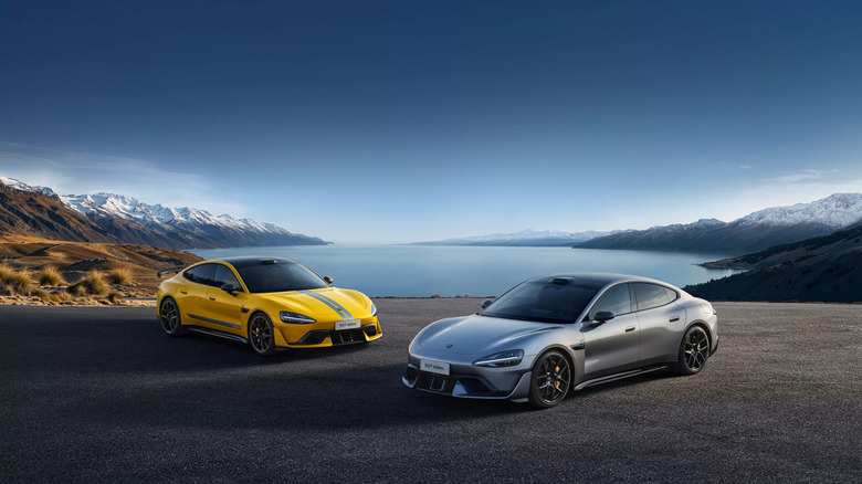 Two Xiaomi SU7 Ultras, model on left in yellow with front-right three-quarter view, model on right silver with front-left three-quarter view, both parked in front of lake