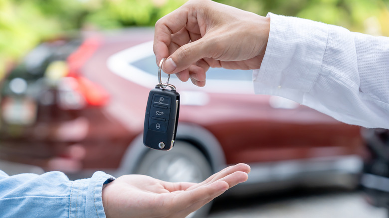 A man handing someone a set of car keys with a red SUV in the background