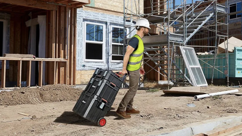 Construction worker pulling Bauer Modular Rolling Toolbox and accessories across job site