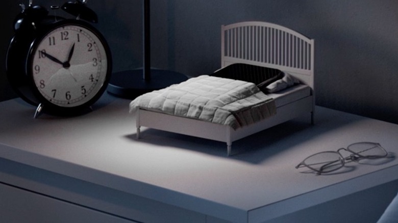 A smartphone tucked into a miniature bed that is part of the IKEA Phone Sleep Collection