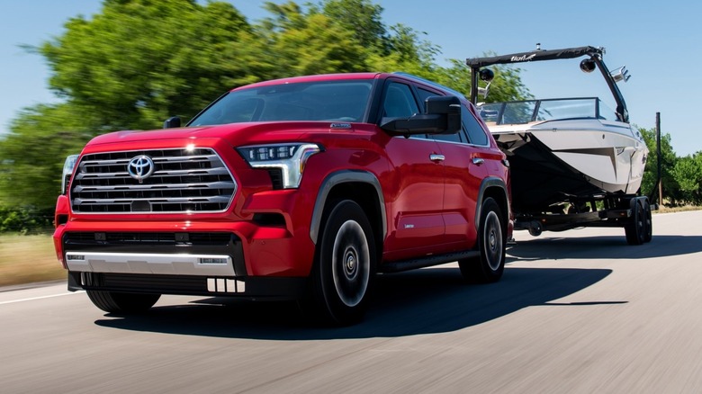 Supersonic Red Toyota Sequoia Limited trim towing a boat with trees in the background