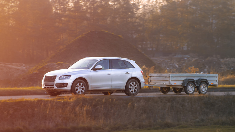 A silver car on a remote road towing a utility trailer