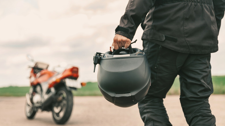 Man walking toward red motorcycle holding helmet in left hand