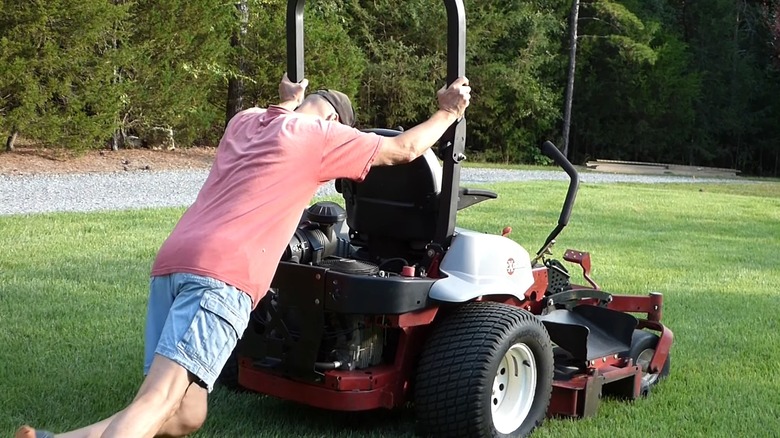 A man pushing a zero-turn mower after it broke down