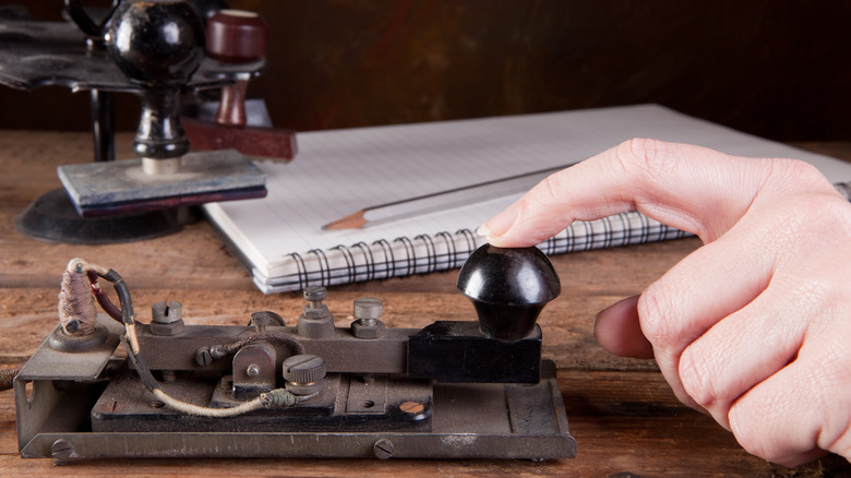 A hand tapping an antique telegraph machine