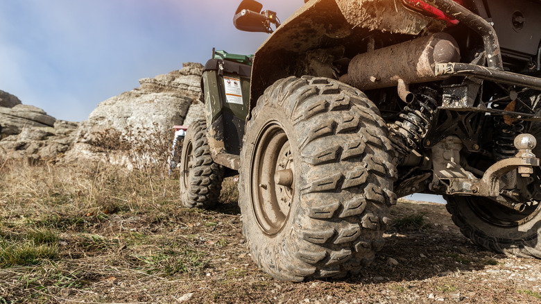 A closeup of a dirty ATV's tires on a grass trail