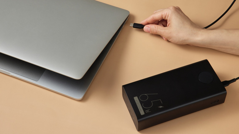 A hand connecting power bank to a laptop