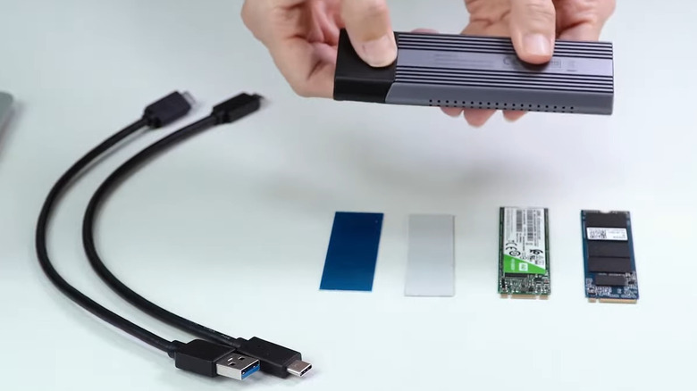 Hands holding SSD enclosure with cables and SSD on table