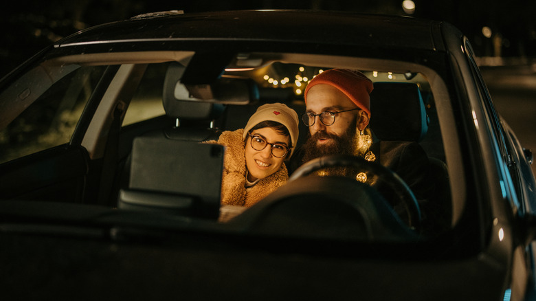Smiling couple sitting in car at night while they watching movie