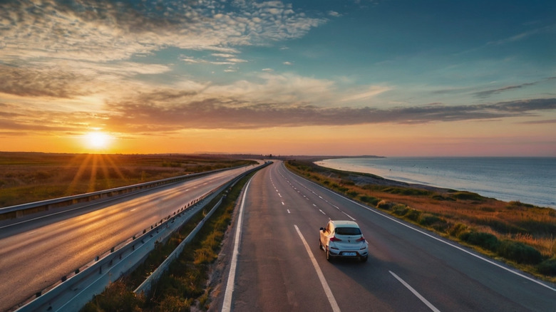 A car driving on an empty coastal highway as the sun sets.