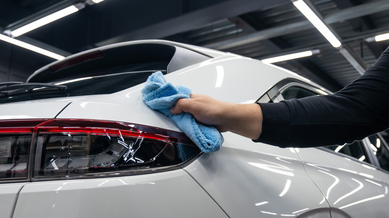 A person using a blue microfiber cloth to wipe a white unidentified car