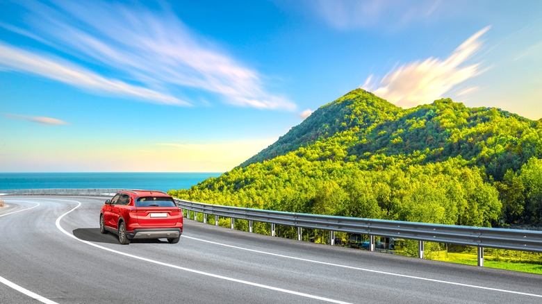 Red SUV driving along coastal road, rear-view