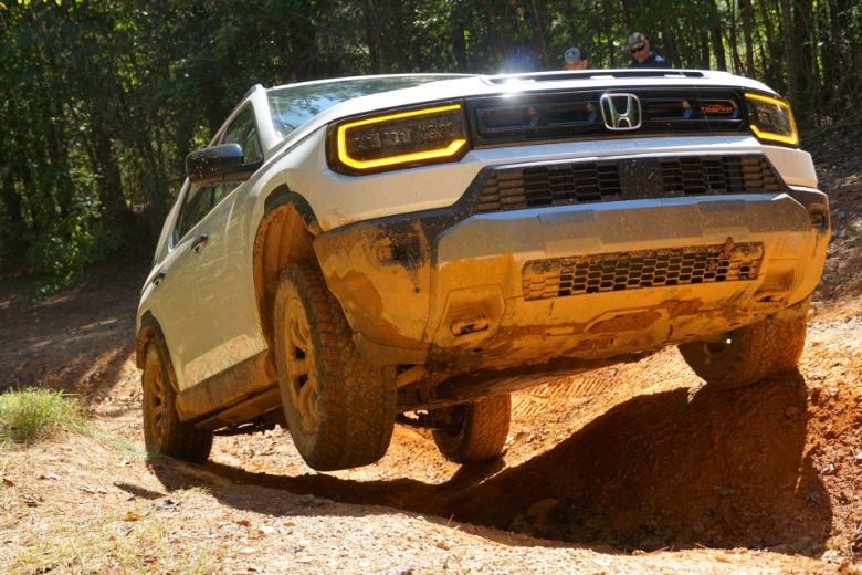 A 2026 Honda Passport TrailSport Elite climbs over a ditch in the trail with the right front wheel up in the air