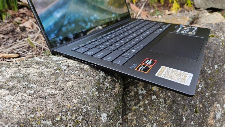 Zenbook 14 OLED 2024 on rocks with the lid open showing off the I/O ports on the left side.